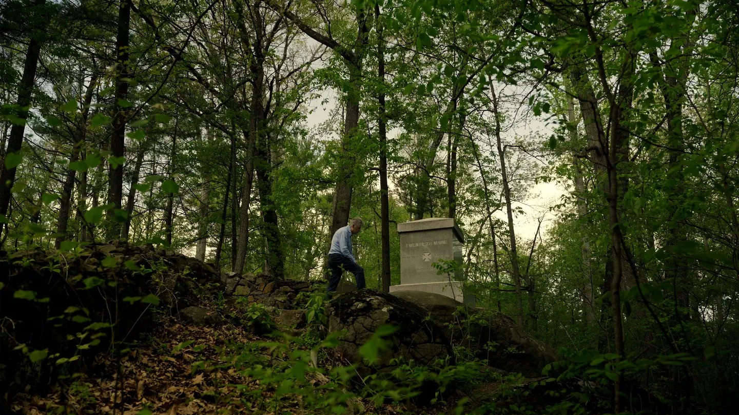 A man climbs toward the Twentieth Maine monument in the woods of Little Round Top.