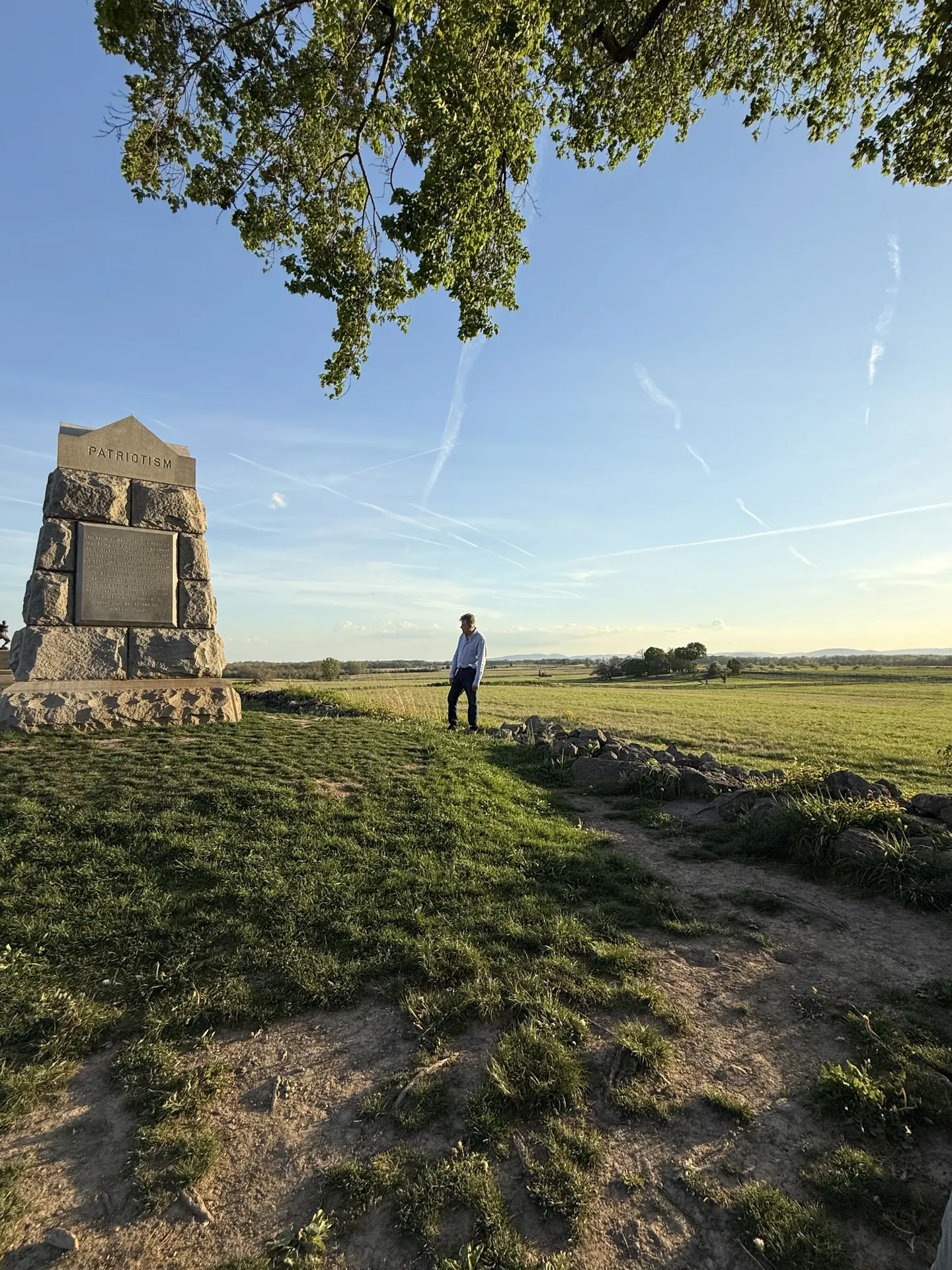 A man stands beside the Patriotism monument overlooking the fields.