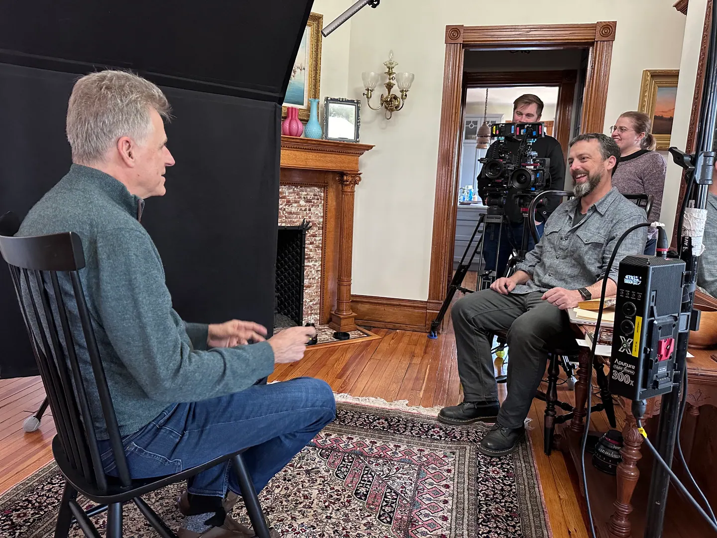 Interview in a parlor with crew and cameras looking on.