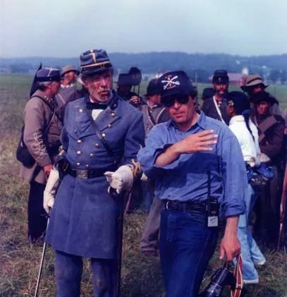 An actor in Confederate uniform beside the director on set, with costumed extras behind.
