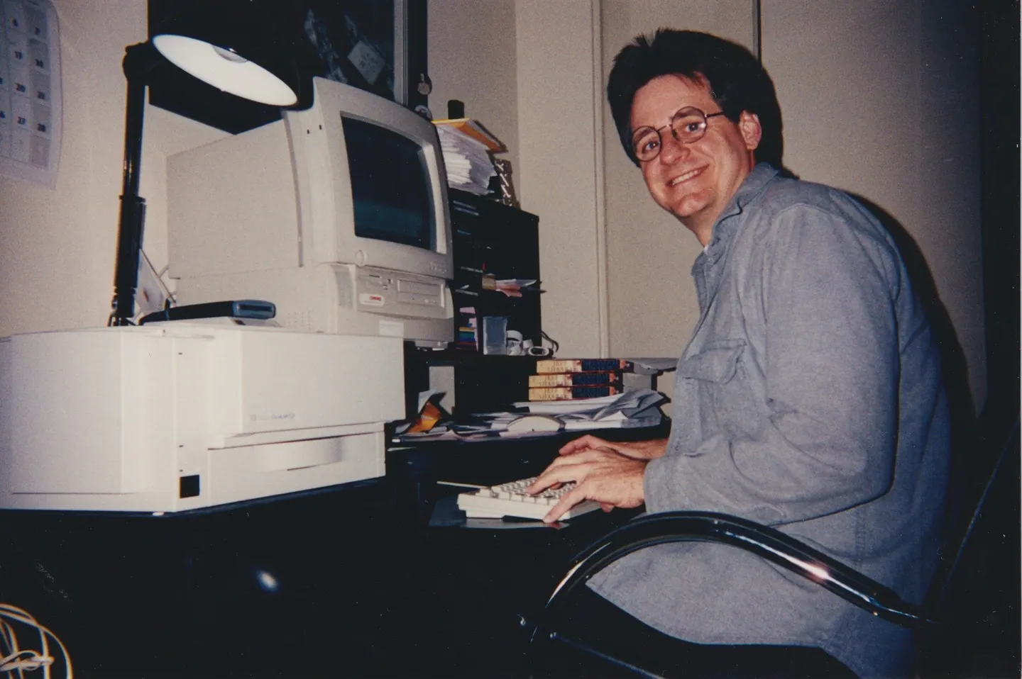 Jeff Shaara smiling over his shoulder while typing at a desktop computer, copies of his novel stacked on the desk.